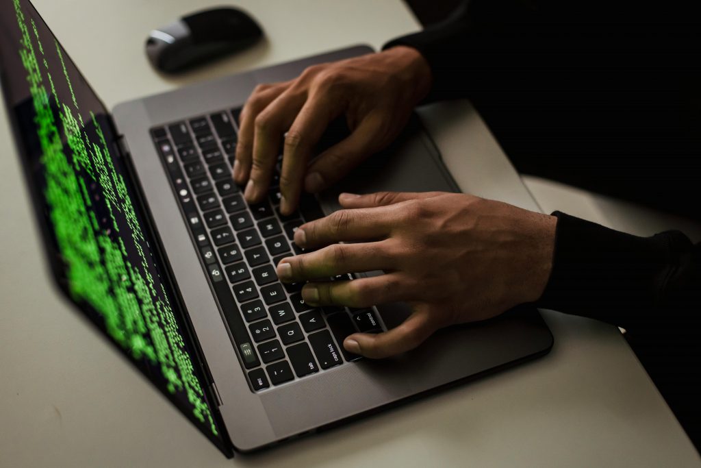 pexels-photo-5935794-5935794 From above of crop anonymous male hacker typing on netbook with data on screen while sitting at desk